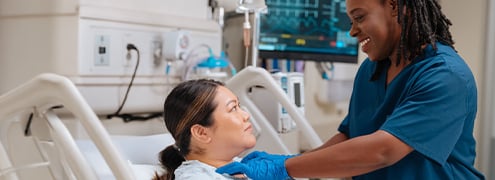A hospital worker checking a patients pulse as she sits in a hospital bed