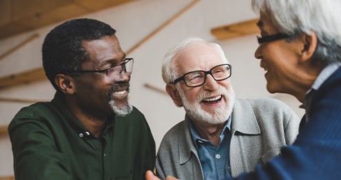 Three older adults engaged in conversation around a table in a welcoming indoor setting, highlighting social connection, community engagement, relationship building, and healthy aging.