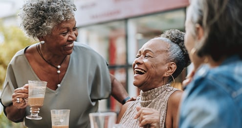 Older adults gathered around a table enjoying beverages and conversation in an outdoor community setting, highlighting social connection, resident engagement, wellbeing, and meaningful shared experiences.