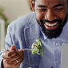 A man eats a salad while focused on his laptop screen, combining healthy eating with work or study.
