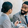 A man and woman enjoying a meal together at an outdoor table, surrounded by greenery and a sunny atmosphere.