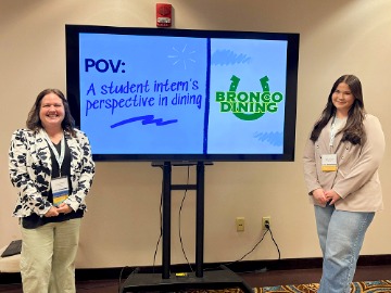 SUNY Delhi Bronco Dining Marketing Director Tracey Stefanelli and student intern Laurel Brigham smiling in front of a presentation screen. 