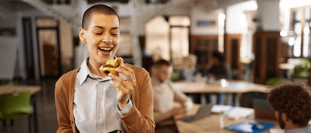 Person holding a pastry in a spacious, well-lit office with people working in the background.