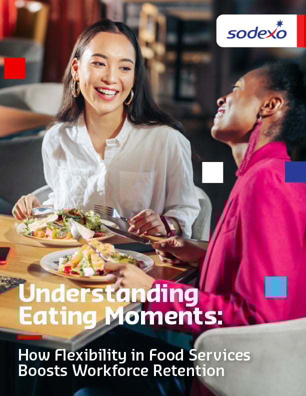 Two people sitting at a table with plates of salad and bread, holding utensils, with a phone placed nearby.