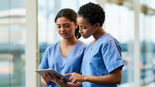 Two dietetics professionals in blue scrubs looking at a tablet together. 