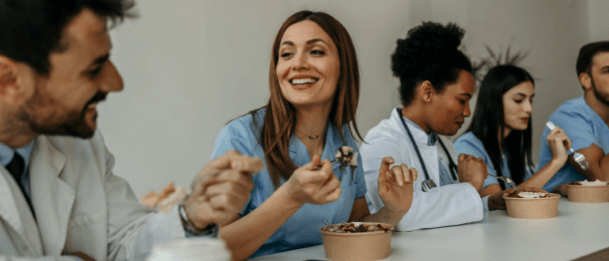 Healthcare workers sitting together at a table eating meals from bowls.
