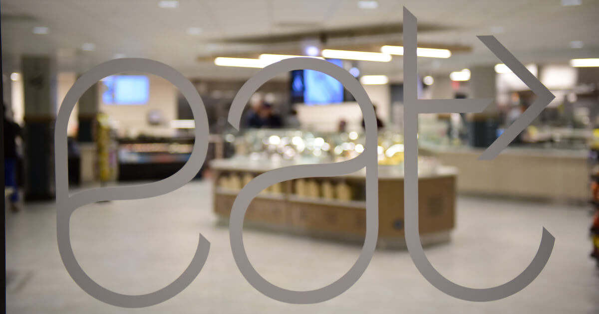 Frosted glass door with the word “eat” stylized, showing a cafeteria interior in the background.