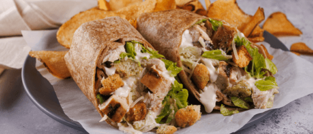 Chicken Caesar wrap cut in half on a plate with chips.