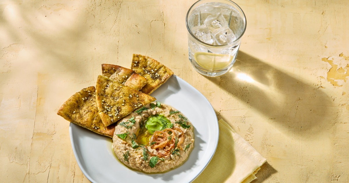 Hummus with pita wedges on a white plate, beside a glass of lemon water.