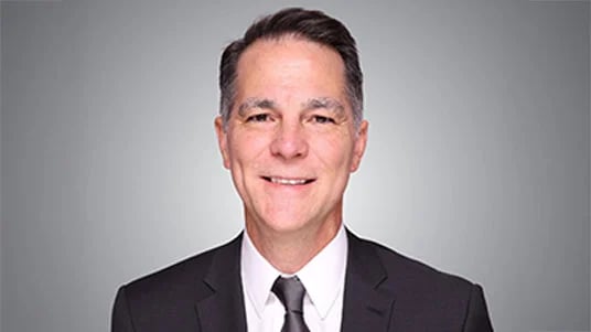 Jason Usie - National Director, GPO Strategy, smiling wearing a black suit, white shirt and dark tie on gray gradient backdrop.