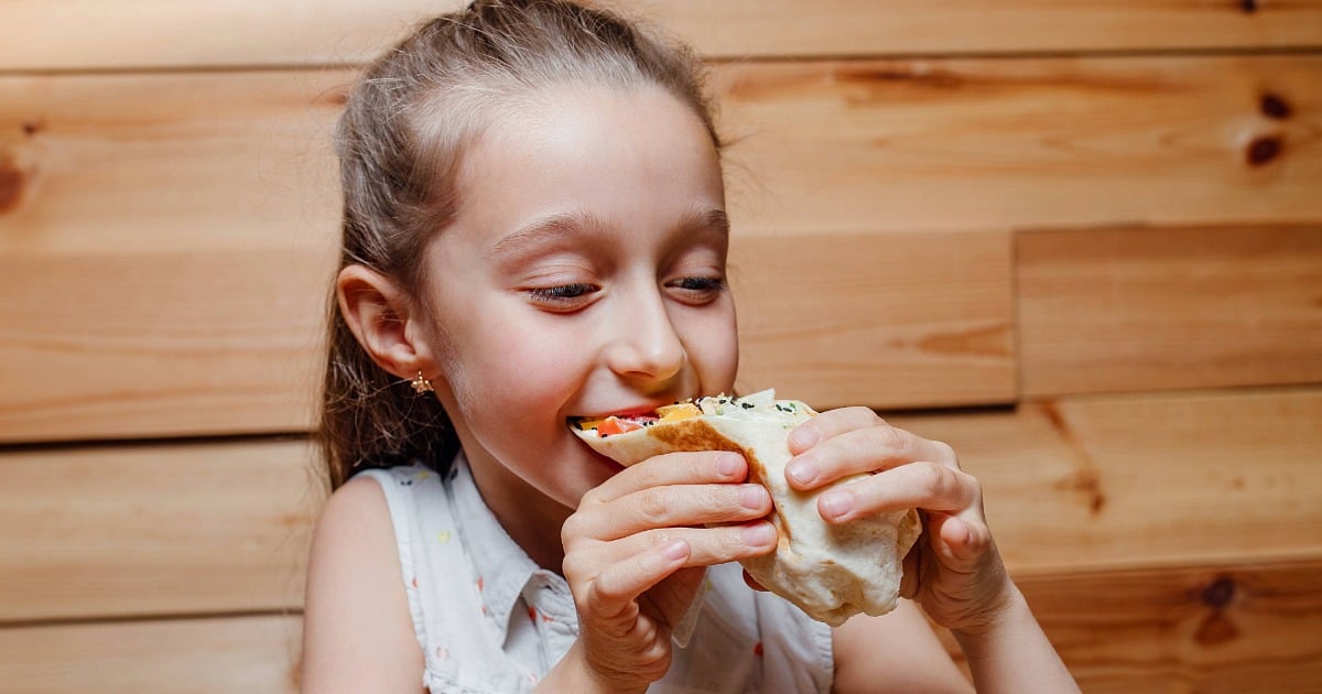 A young student smiling while eating a wrap-style meal, representing healthy and enjoyable school dining.