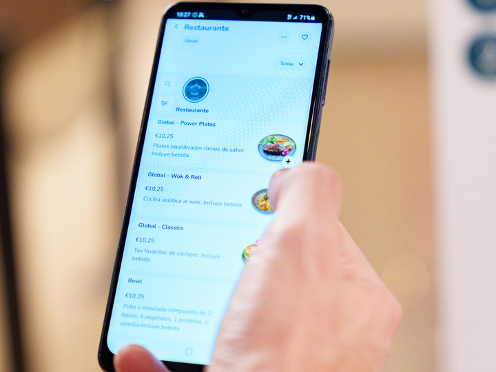 Hand holding a smartphone showing a restaurant menu app with meal options, prices, and photos on the screen.