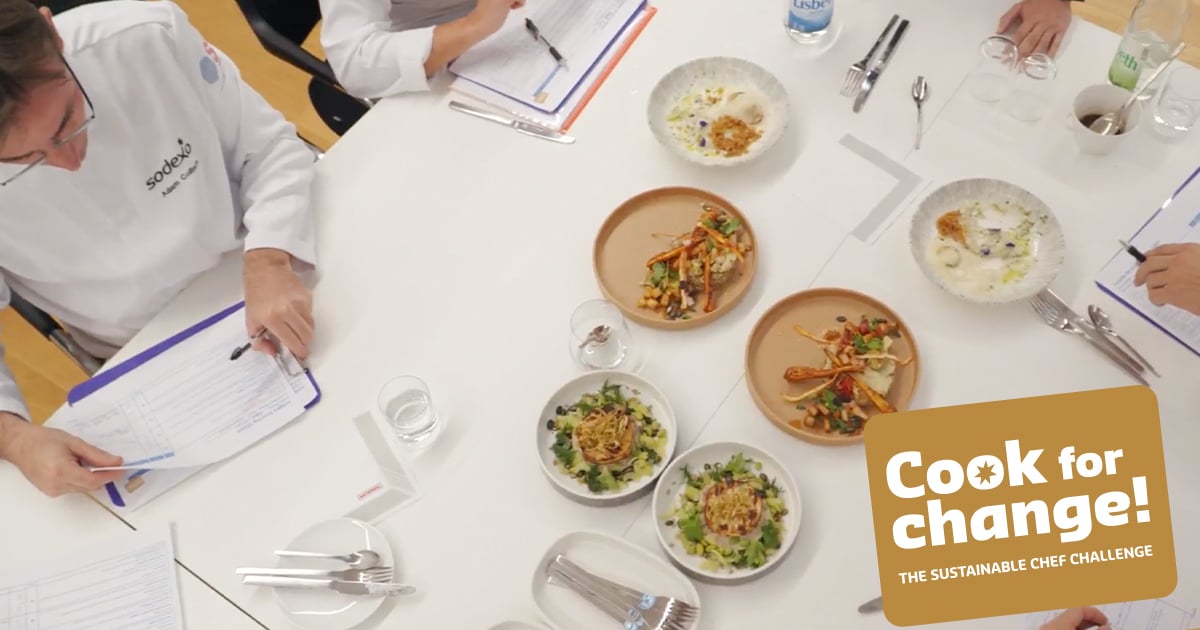 Chefs seated around a table evaluating plated dishes, with notebooks, utensils, and glasses arranged neatly, alongside a ‘Cook for Change! The Sustainable Chef Challenge’ graphic.