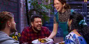 A group of people gathered around a table, enjoying a meal with various plates of food in front of them.