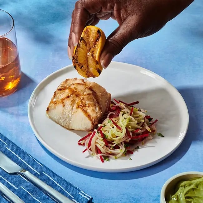 Lemon being squeezed over a gourmet fish dish
