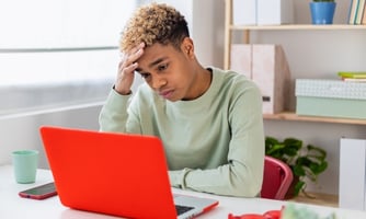 Stressed student with hand on forehead, staring at a laptop