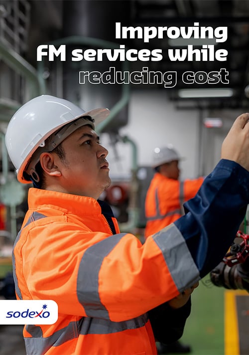 Facilities management promotional graphic featuring industrial workers in safety gear performing equipment maintenance inside a manufacturing facility, highlighting operational efficiency and cost reduction initiatives.