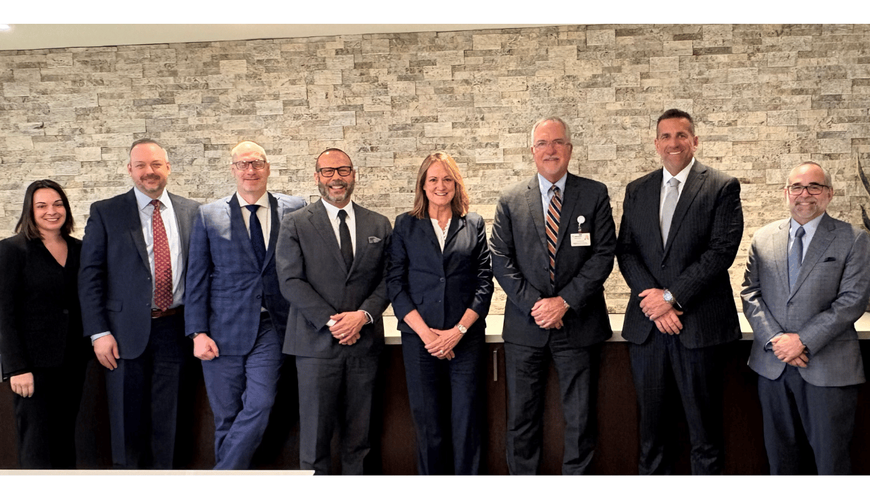 Eight business professionals standing in a lobby against a textured stone wall, posing for a group photo.