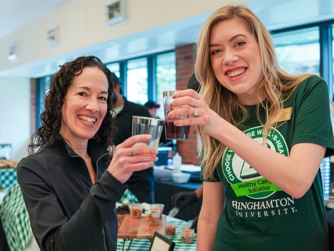 Two Binghamton dietitians smiling and holding up drinks at a campus event. 