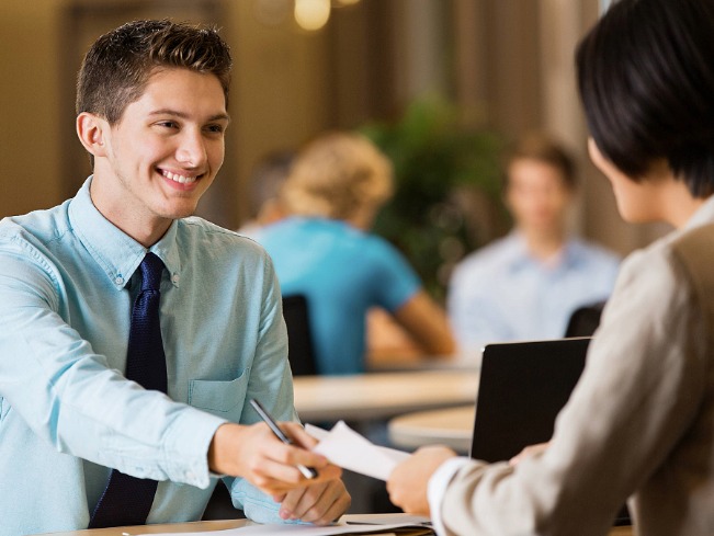 College student in professional attire handing a resume to a recruiter at a campus career fair.