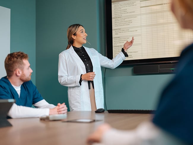 Healthcare professional presenting information on a large display while colleagues attend a meeting.