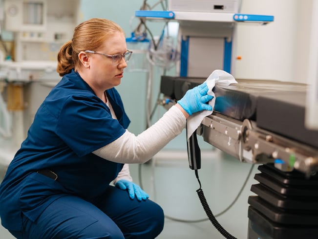 Healthcare environmental services professional disinfecting a patient treatment table in a clinical setting, highlighting infection prevention, hospital sanitation, patient safety, and healthcare facility cleanliness.