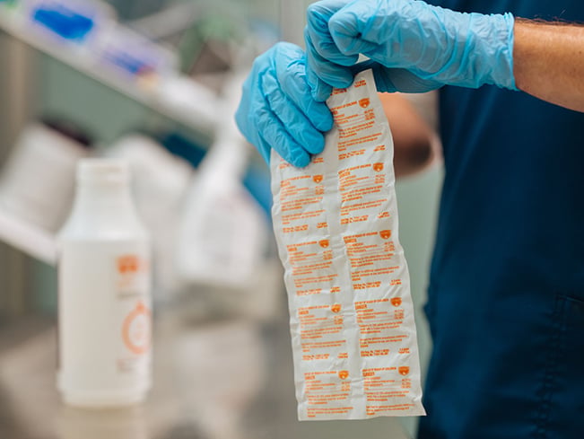 Close-up of gloved hands handling individually packaged cleaning products in a healthcare environment, highlighting infection prevention, sanitation protocols, supply management, and hospital hygiene practices.