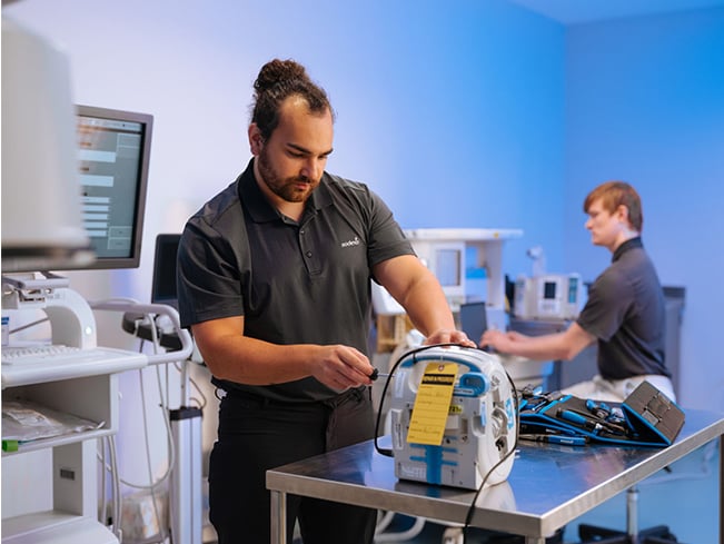 Healthcare technicians performing maintenance and testing on medical equipment in a clinical technology workspace, highlighting biomedical services, equipment reliability, standardization, and healthcare operations support.