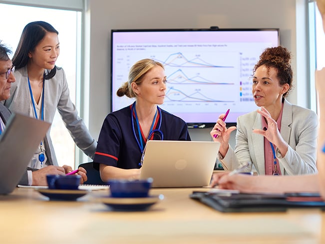 Healthcare team discussing patient care and reviewing data during a meeting with charts on a screen.