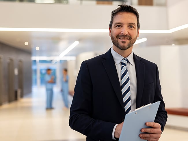 Professional holding a clipboard in a modern healthcare facility hallway.