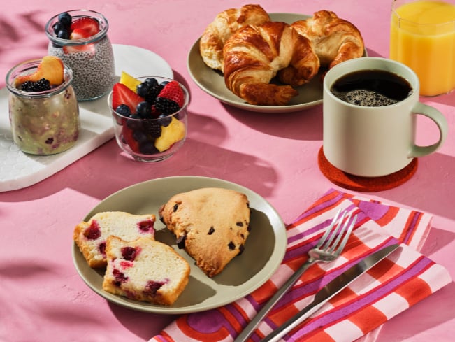 Assortment of breakfast items including croissants, berry parfaits, fruit cups, coffee, orange juice, and baked pastries arranged on a colorful table, highlighting variety, choice, and enjoyable dining experiences.