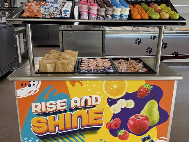 School breakfast station stocked with fruit, milk, juice, snacks, and grab-and-go meal options.