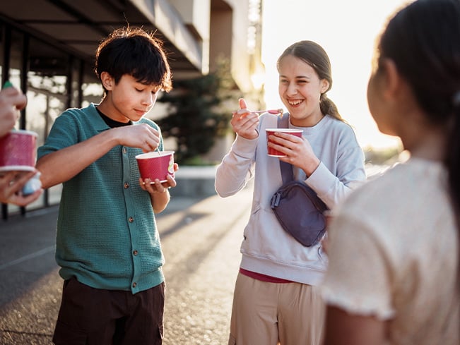 Students enjoying frozen treats outdoors near a school campus during an afternoon break