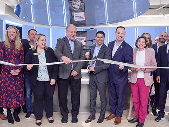 A group of people cutting a ribbon together in a well-lit room, celebrating a special event or opening.