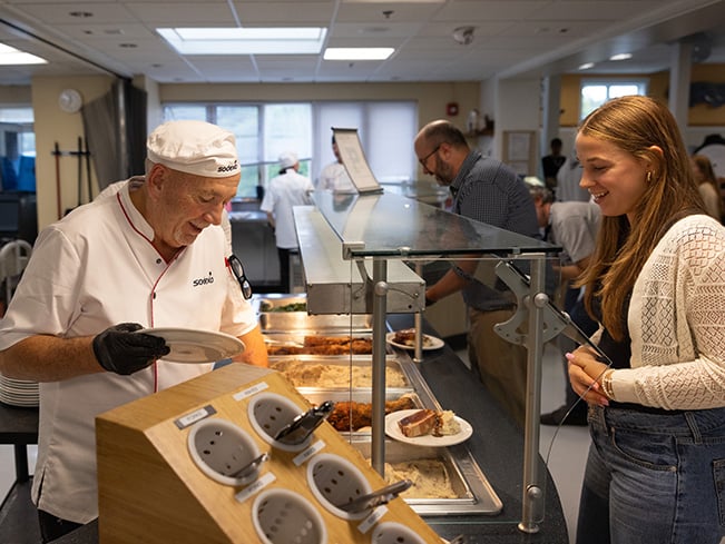 Food service worker serves cafeteria meal to customer at a hot buffet counter.