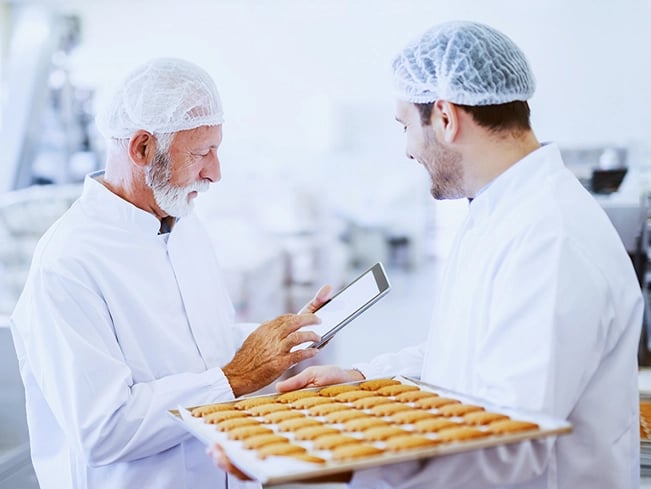 Two men wearing white lab coats stand together, likely in a laboratory setting, engaged in discussion or collaboration.