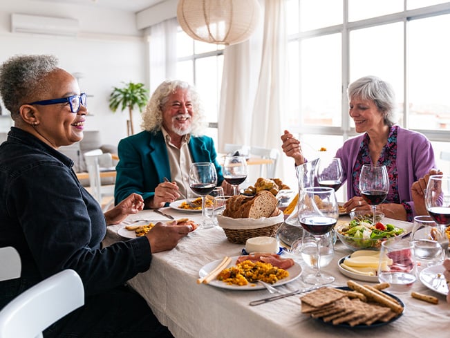 Older adults gathered around a dining table enjoying a shared meal with wine, salads, and freshly prepared dishes, highlighting social connection, hospitality, community living, and wellness-focused dining experiences.