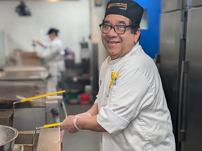 A SUNY New Paltz dining team member smiles while cooking in the campus dining kitchen.