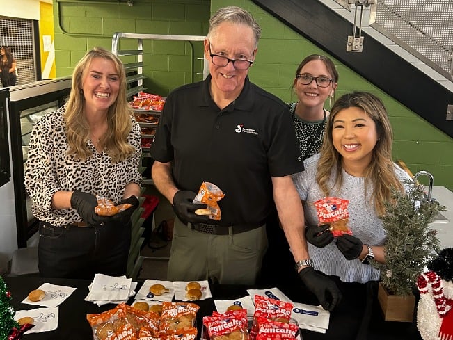 Smiling school staff with trays of different pancake puff snack flavors for a student taste test. 