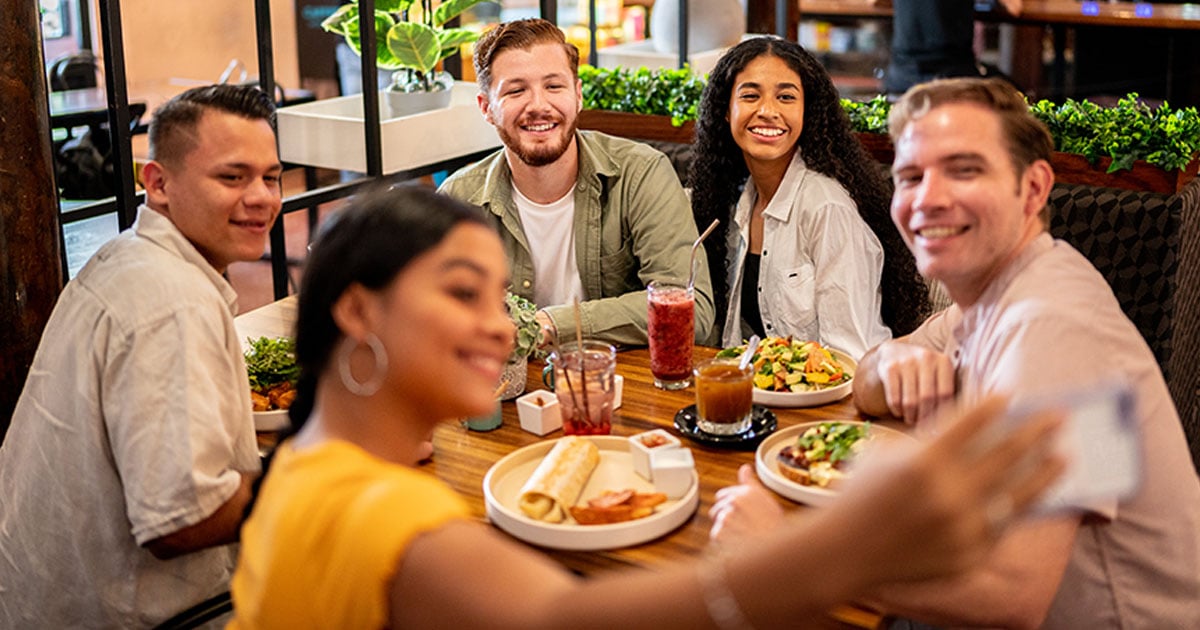 Group of university students sharing a meal while taking a selfie together, highlighting social connection through campus dining.