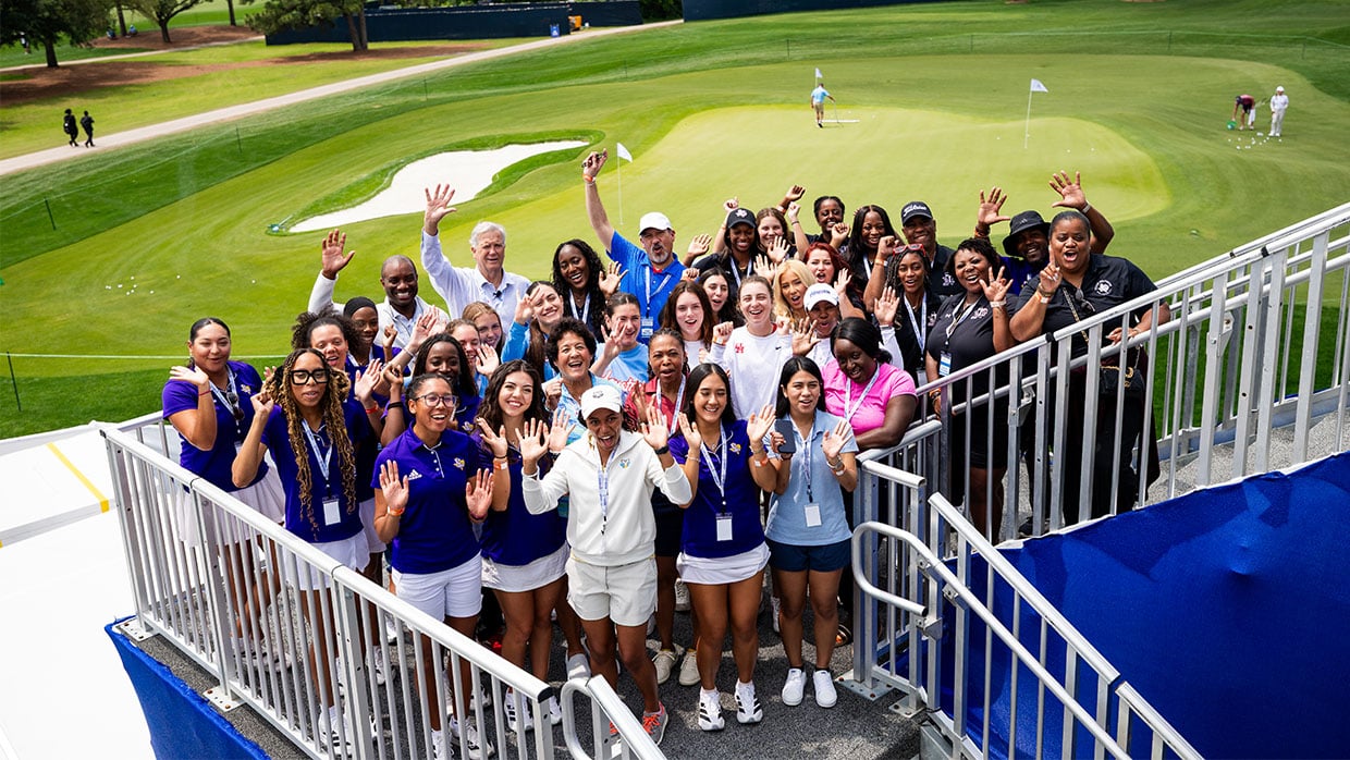 Group of attendees waving from stadium steps overlooking a golf course practice green.