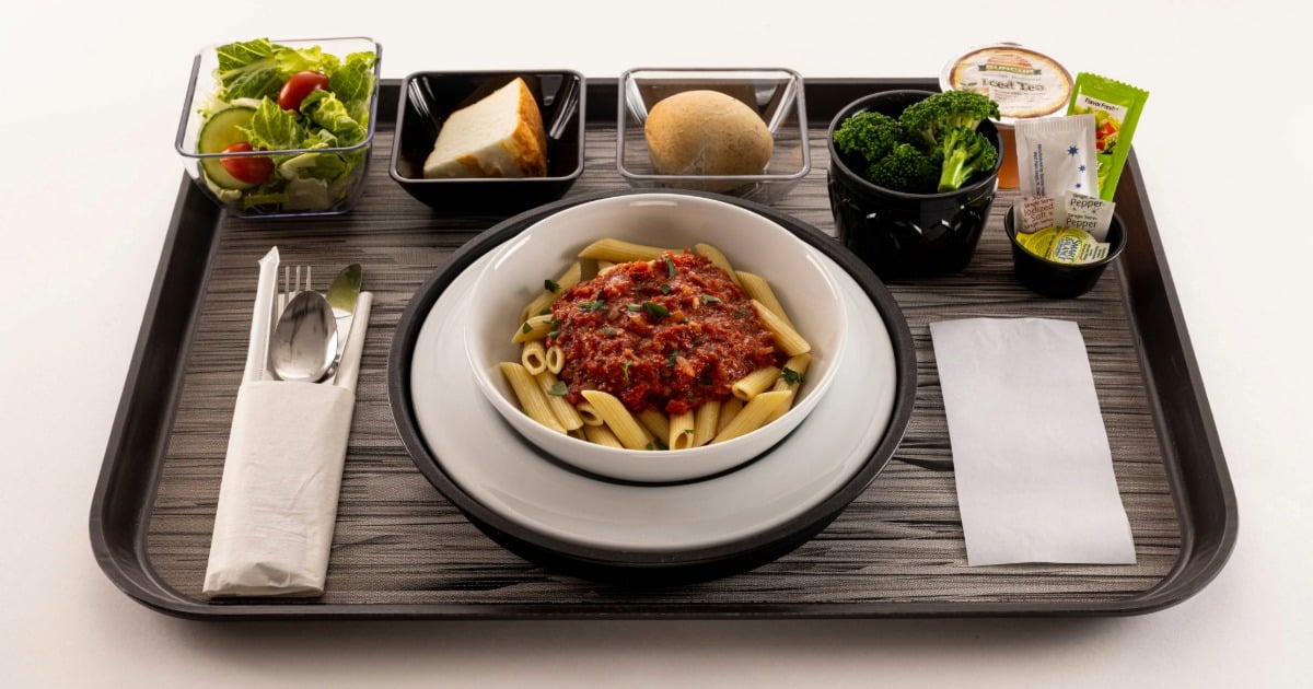 Top-down view of a Clinicia patient menu meal, featuring penne pasta marinara, a fresh side salad and a serving of broccoli on a hospital tray.