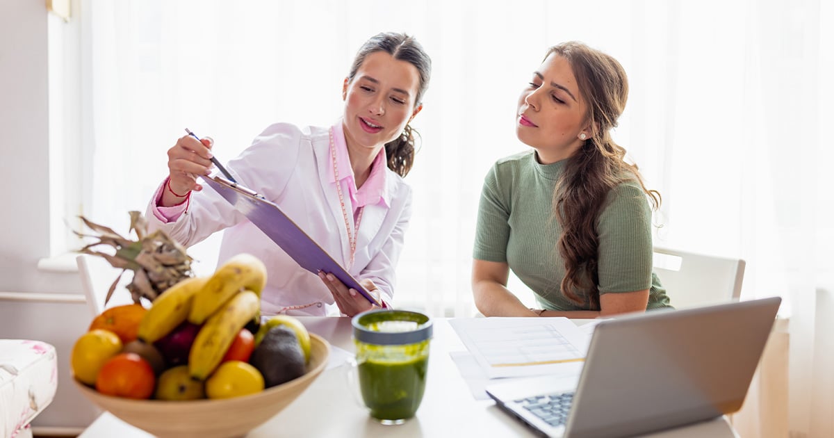 Registered dietitian consulting with a client at a table with fresh fruit, a green smoothie, and a laptop, providing personalized nutrition guidance, wellness support, and healthy eating recommendations.