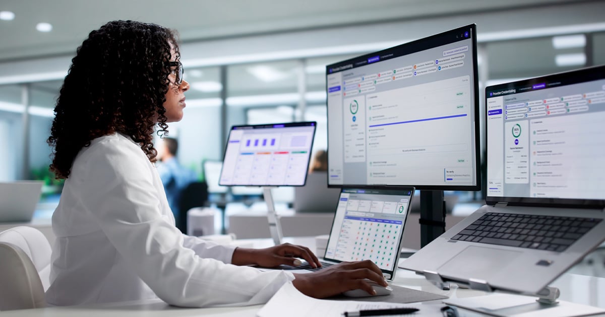 Healthcare professional using multiple monitors to manage digital healthcare operations and data.