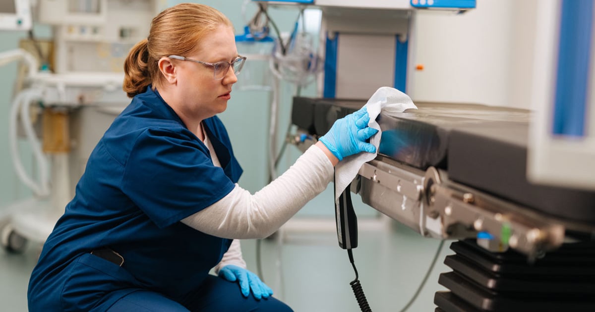 Healthcare environmental services professional disinfecting medical equipment in a clinical treatment room, highlighting infection prevention, hospital sanitation, patient safety, and healthcare facility cleanliness.