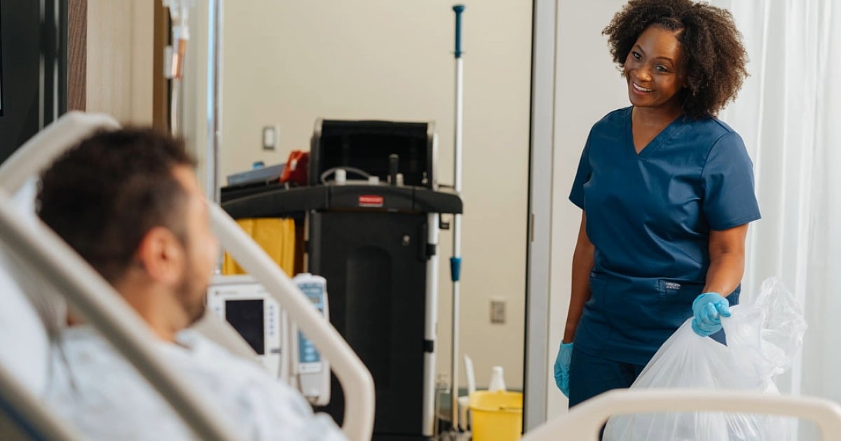 EVS attendant cleaning a hospital room and engaging with a patient.