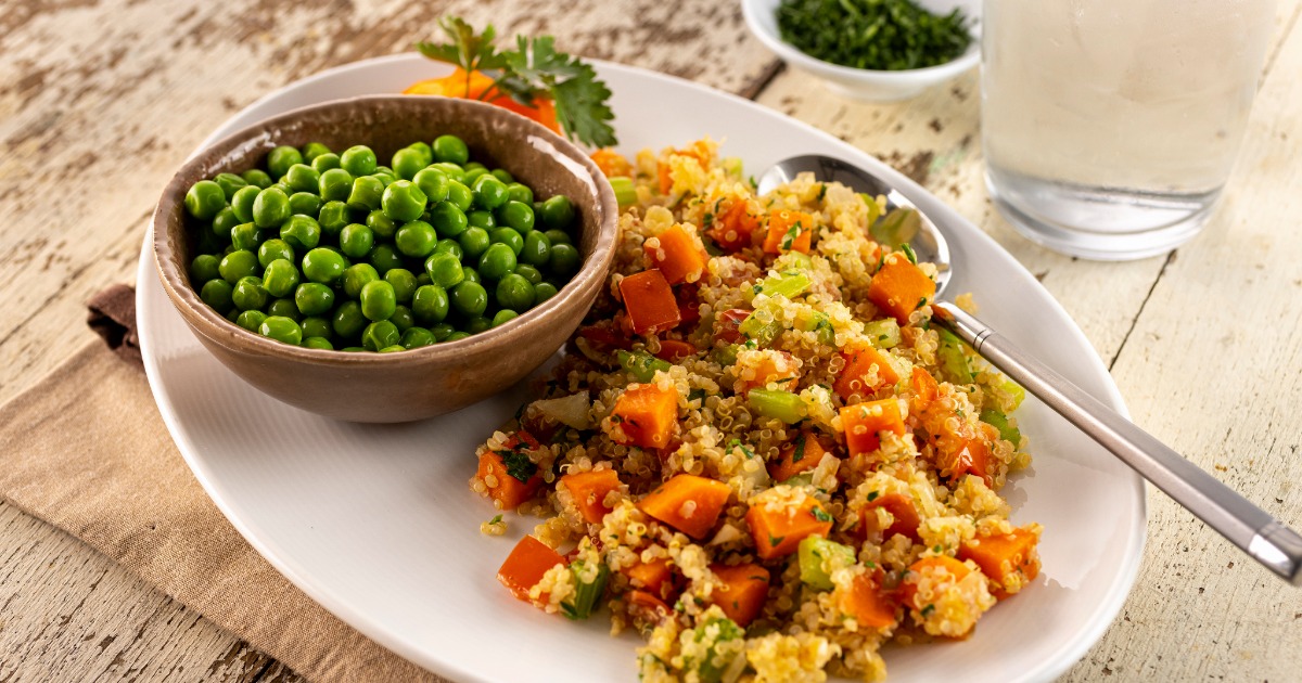 A plant-based quinoa primavera garnished with fresh herbs, served with a side of peas and a glass of water. 