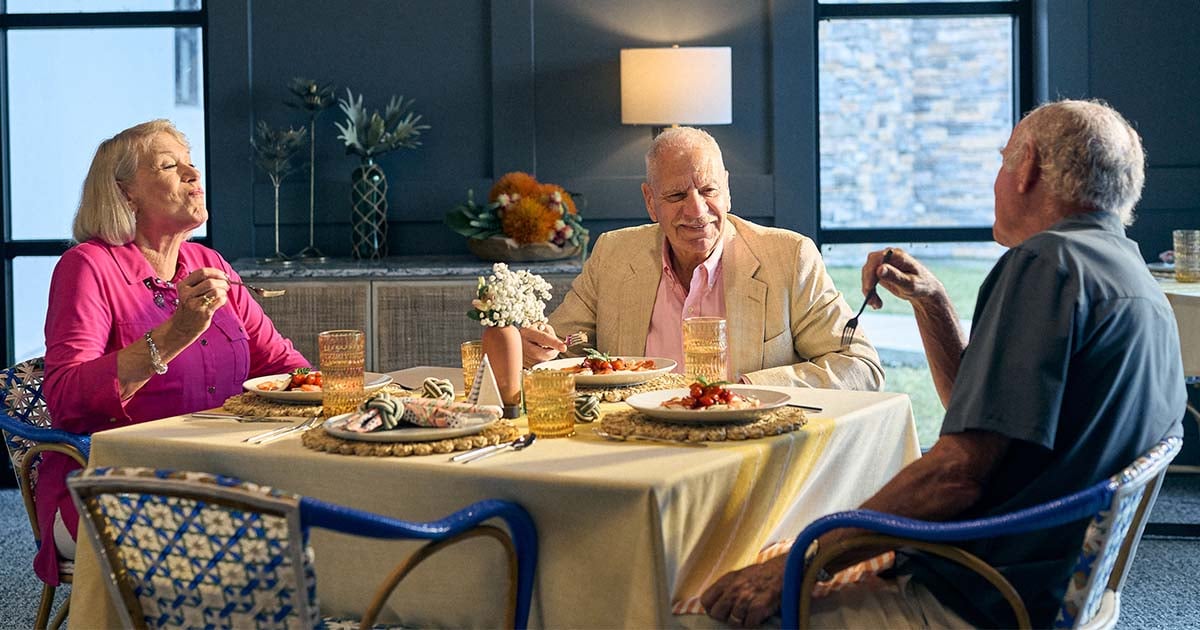 Older adults seated around a dining table enjoying a shared meal in a welcoming community setting, highlighting social engagement, hospitality, resident wellbeing, and meaningful dining experiences.