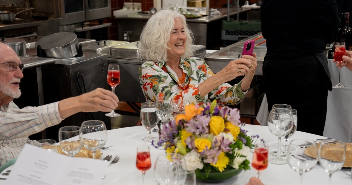 Senior residents celebrating at a community dining event, raising glasses around a table with flowers.