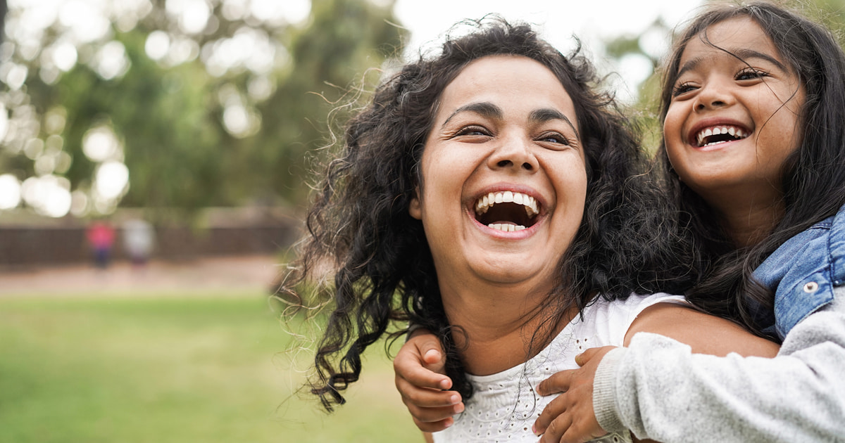 Two individuals outdoors, one giving a piggyback ride on a grassy area.